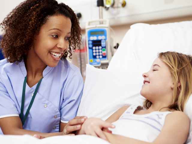 A female nurse smiling and talking to a young girl patient that's resting on a hospital bed.  The College will enroll its first BSN class in the spring of 2018.