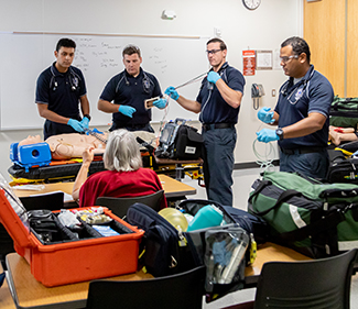 Paramedic students working together in a lab session in a classroom and listening to the professor's instructons