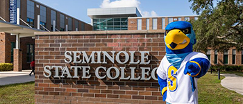 Rally the Raider mascot standing in front of the Seminole State College brick sign at the Student Union building on the Sanford/Lake Mary campus